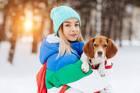在冬季公园里, 穿着温暖时尚的衣服, 穿着背包摆姿势的时髦年轻女子的肖像。友谊宠物和人类