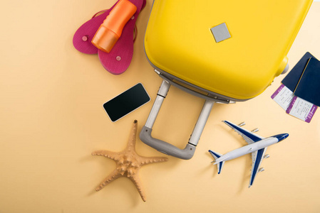 黄色手提箱飞机模型海星防晒拖鞋智能手机和米色背景票的顶部视图