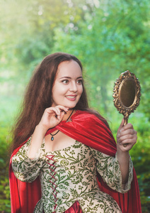 美丽的微笑的女人，穿着中世纪的长裙，带着镜子户外