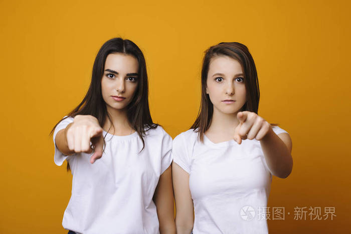两个黑发白种人女孩的肖像严肃地指着你对着一堵黄色的墙