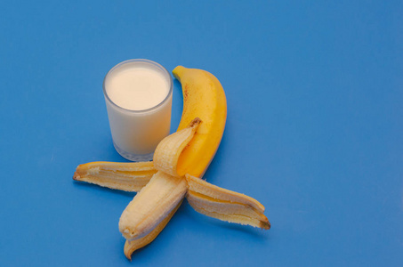 成熟的香蕉和一杯蓝色背景的酸奶。健康饮食的概念