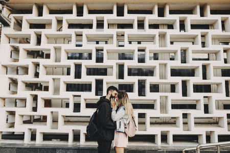 美丽的白种人夫妇在外面约会时，拥抱和亲吻在一堵惊人的墙前。