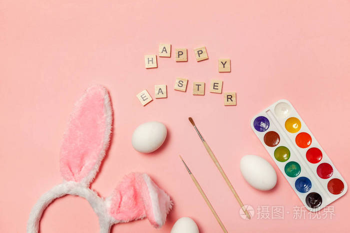 复活节快乐。为假期做准备。铭文HappyEaster字母，鸡蛋，彩色油漆和兔子耳朵隔离在时尚的粉红色背景。简约简约简约平面，俯视