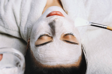 美丽的欧洲妇女有面部皮肤程序，通过应用白色年轻化面具由美容师。