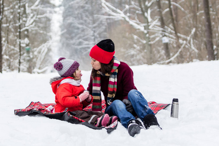 母亲和孩子女孩在下雪的冬天在大自然中散步，玩得开心，喝茶。 冬季概念。