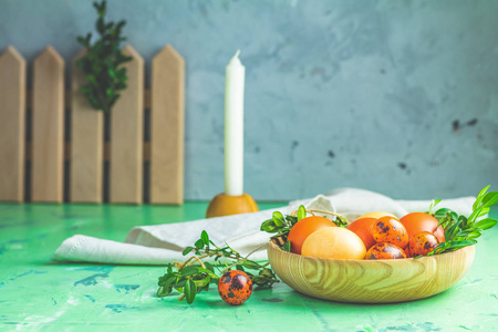 复活节贺卡与彩色黄色橙色鸡蛋与鹌鹑鸡蛋和绿色树枝在木制盘子上的绿色混凝土表面背景。 复制空间。 调色图像