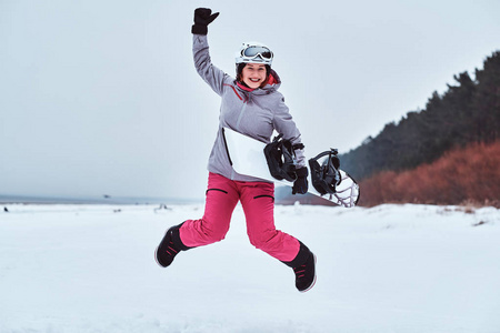 愉快的妇女穿着温暖的运动服跳与滑雪板在雪海滩上