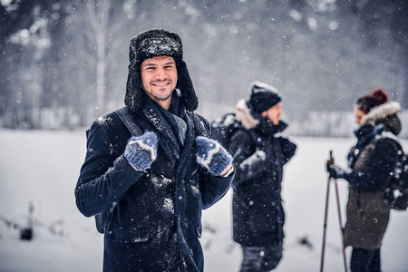 一个带着背包的微笑的徒步者的肖像, 他和他的朋友们一起在冬天的森林里散步