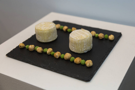 两个托米诺奶酪在黑色桌布上装饰着豌豆和鹰嘴豆。