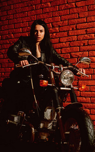 骑摩托车。的女人骑摩托车。骑摩托车的女车手。女孩骑摩托车在砖墙上