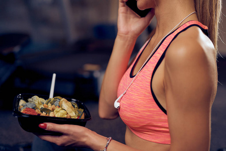 关闭妇女使用智能手机，同时持有健康食品在另一方面。 健身房内部健康生活方式理念。
