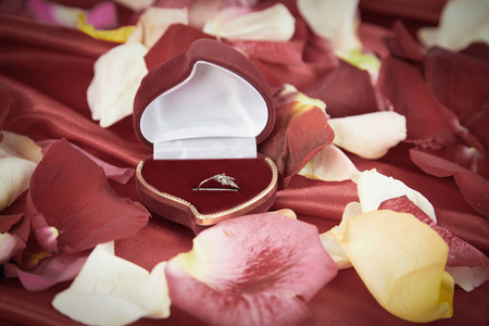 钻石戒指和玫瑰花瓣在明亮的红色背景