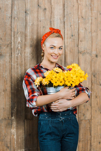幸福的女人拿着桶里的花，在木栅栏边微笑