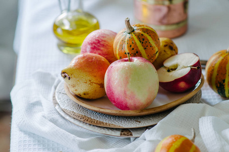 平静的生活，小南瓜，苹果和梨在陶瓷盘子里。秋天仍然生活在明亮的色彩中。桌上的蔬菜水果搭配白色桌布..