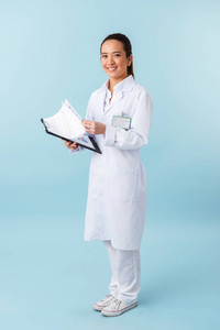 照片的一个快乐的年轻女医生摆在蓝色墙壁背景上，手持剪贴板。