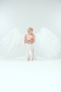 美丽的年轻女子，有天使的翅膀，遮住乳房，同时摆出白色的背景