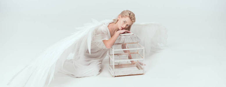 美丽的女人，穿着天使的服装，翅膀靠在鸟笼里，看着白色的摄像机