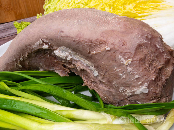 牛舌放在盘子里,上面放着大白菜,樱桃,西红柿和洋葱,上面放着木制背景