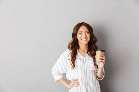 活泼开朗的亚洲女人在灰色背景下孤独地喝咖啡