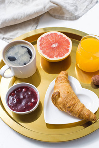 法国早餐在金色托盘咖啡果酱牛角面包橙汁葡萄柚荔枝。 顶部视图白色背景