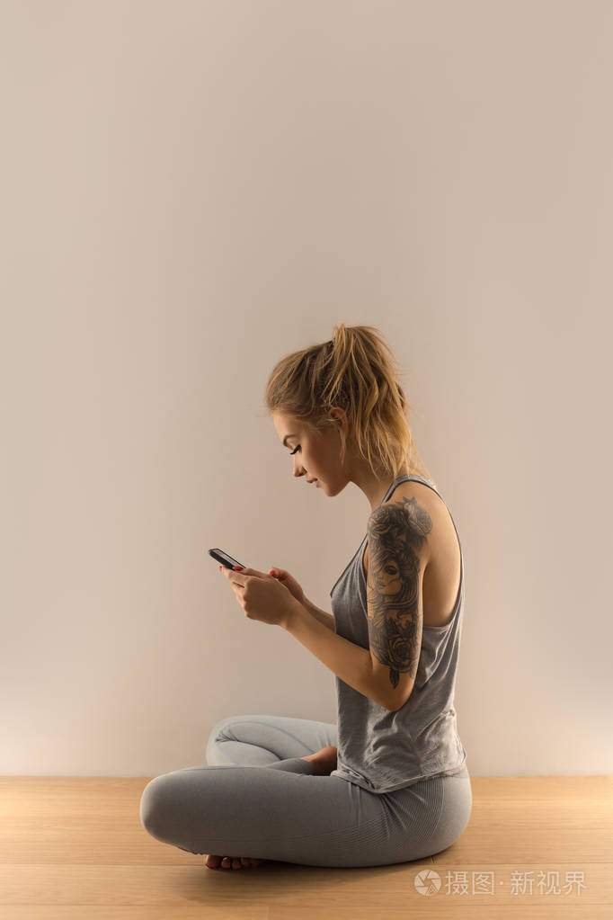坐在室内的带智能手机的运动女性