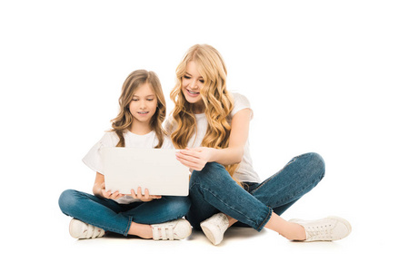 漂亮的女人和可爱的女儿坐在地板上，在白色背景上使用笔记本电脑