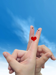 概念或概念人类或女性的双手，用两个手指涂着红色的心，在云蓝色的天空背景上微笑着的脸