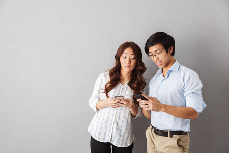 快乐的亚洲夫妇在灰色背景下使用手机被孤立