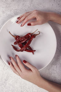 美丽的女性手与暗红色指甲白色背景红色辣椒在盘子上。 指甲延伸。 美甲水疗沙龙。 创意广告。