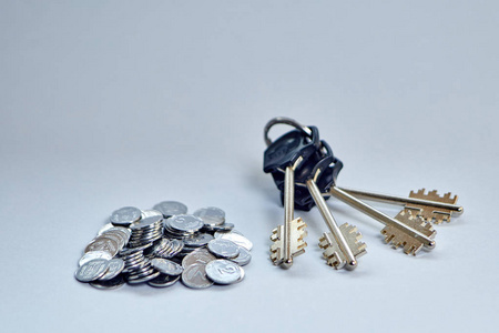 一串钥匙躺在一把硬币旁边，贴在一个浅色的背景上。 把钱保管好