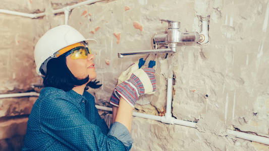 戴手套的女建筑工人用扳手修理浴室的管道。 图像