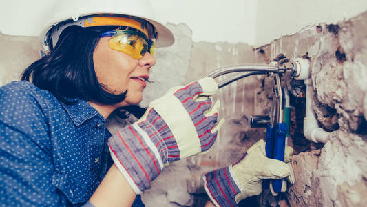 戴手套的女建筑工人用扳手修理浴室的管道。
