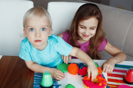 男孩和女孩坐在家里的桌子上玩橡皮泥