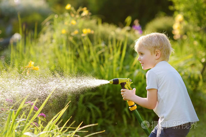 有趣的小男孩在阳光明媚的后院玩花园软管。学龄前儿童享受喷水的乐趣。孩子们的夏季户外活动。