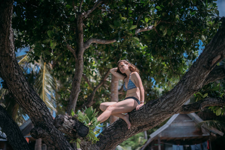 阳光明媚的一天，一个年轻美丽的苗条女人在热带岛屿上的海洋海岸上的一棵树上。