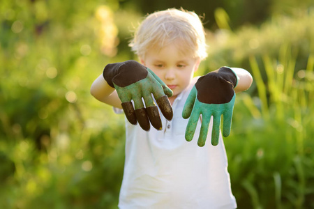小男孩戴着花园手套，在家庭花园工作期间玩得很开心。 有子女家庭的园艺活动