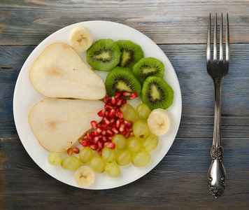 水果混合梨猕猴桃葡萄香蕉石榴在木制背景上。 盘子里的水果