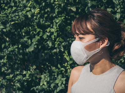 美丽女性戴口罩美丽的亚洲妇女戴白色防护n95防尘口罩在绿叶背景与