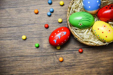 复活节彩蛋放在乡村餐桌上的巢篮里，木制背景彩色彩色彩蛋，上面装饰着彩色糖果糖果。