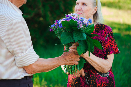 一位80岁的老人在一个夏天的公园里给他的妻子送花.照片