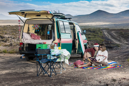 已婚的男人和女人坐在野营车附近的格子布上，读着书享受着西班牙兰萨罗特岛的时光