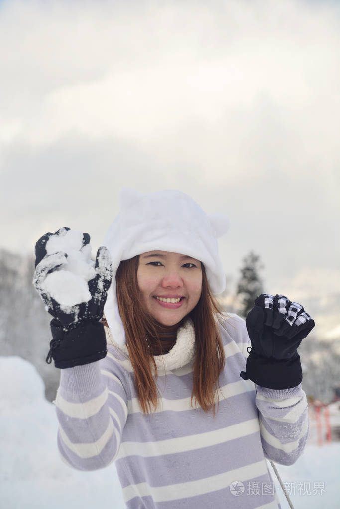 幸福微笑的年轻女子戴着白帽子，双手捧着雪在雪地的背景上。