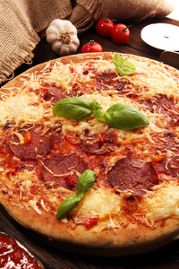 意大利比萨饼，配上意大利香肠和融化的奶酪红色西红柿和绿色罗勒，放在由奶酪番茄和红色樱桃番茄装饰的桌子上。