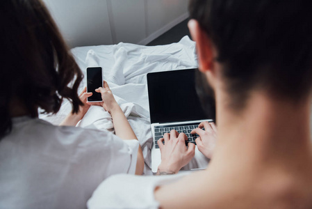 两对夫妇躺在床上，同时使用笔记本电脑和智能手机，家里有空白屏幕