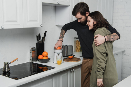 一对漂亮的年轻夫妇在厨房里做橙汁和拥抱