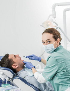 牙科医生在牙科诊所与病人合作时，持口罩持牙钻