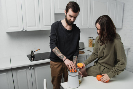 一对漂亮的年轻夫妇在厨房早餐时准备橙汁