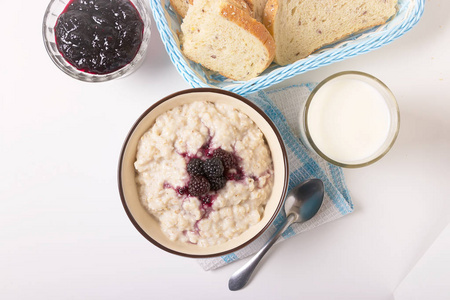健康早餐，一杯牛奶，自制燕麦片，蓝莓在一个蓝色的碗和新鲜的谷类食品面包在一个淡淡的背景。