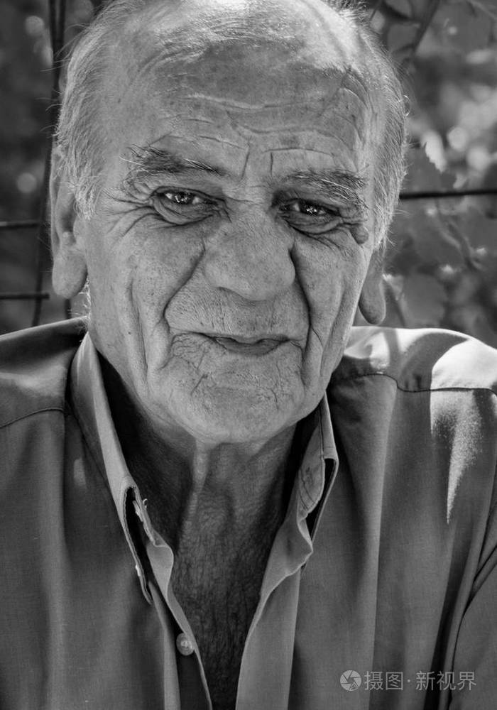 一位严肃的希腊退休男性的特写肖像,他微笑着抽着烟