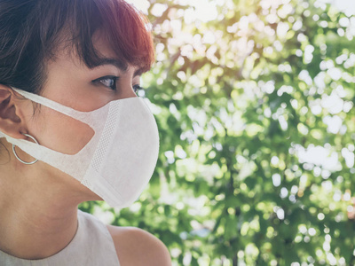 关闭美丽的亚洲妇女戴白色防护N95防尘口罩在绿叶背景与复制空间。 防止污染的概念。